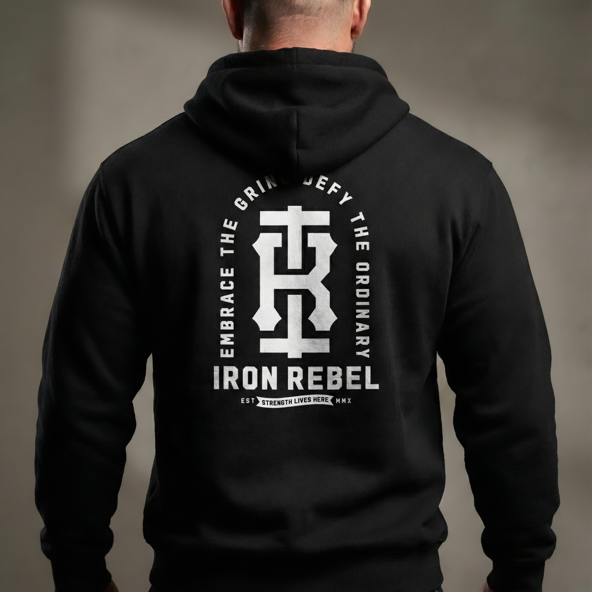 Back view of Iron Rebel black pullover hoodie for men featuring large monolith logo and “Embrace the Grind, Defy the Ordinary” graphic, heavyweight strength training sweatshirt worn by model